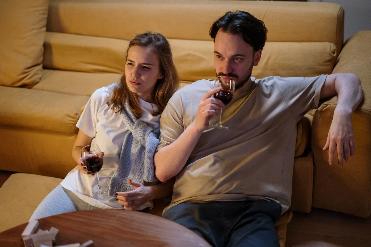 A couple sitting together on a living room floor in the evening, both looking away from each other