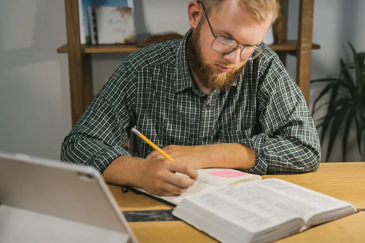 A man at a desk studying an open reference book and making notes
