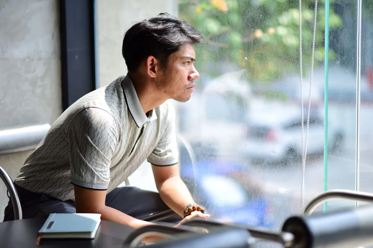 A man sitting alone by a window with a notebook, looking out at the street