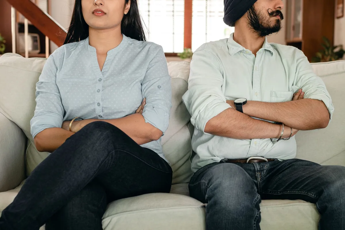 A couple sitting apart on a sofa in tense silence, an image of betrayal trauma in marriage