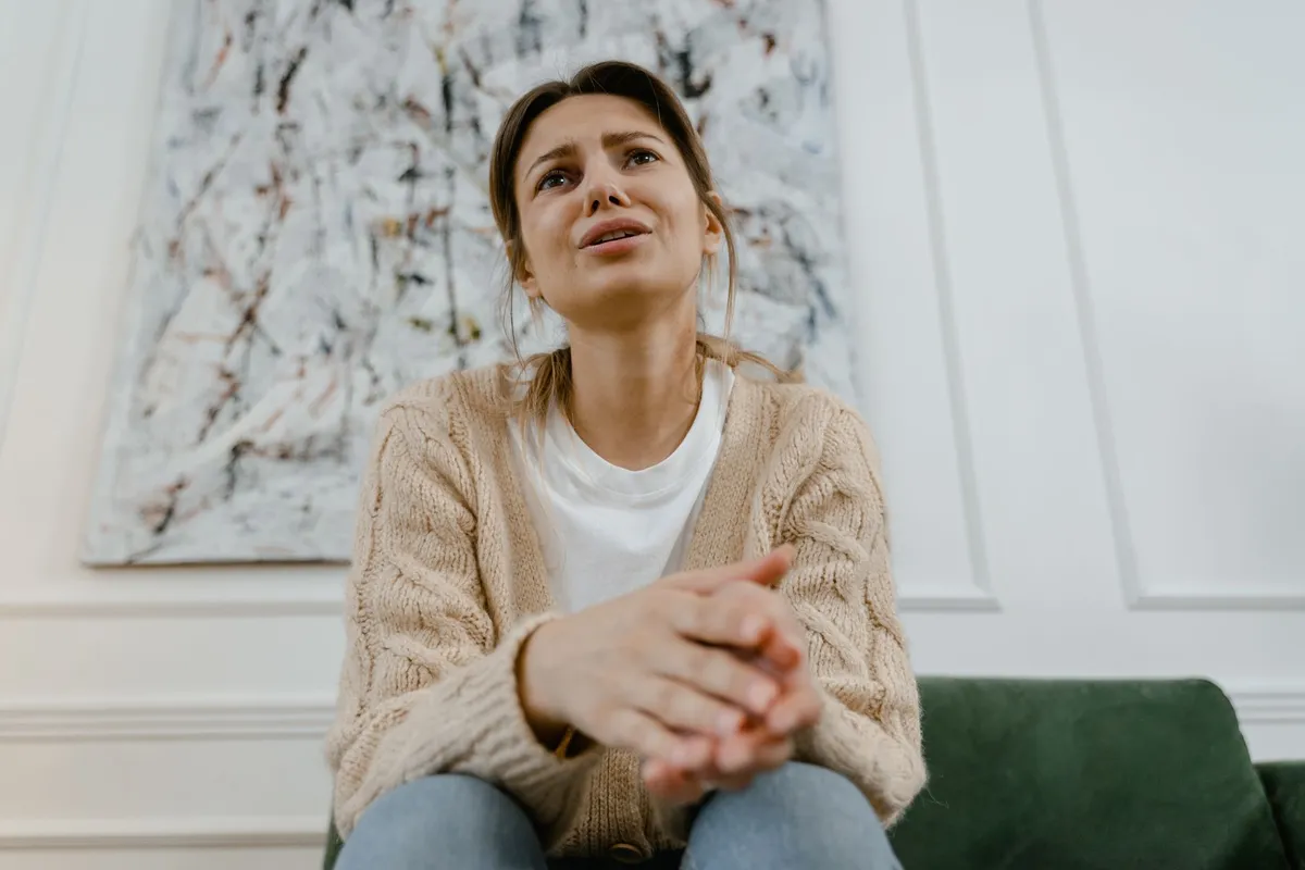 A woman sitting alone with clasped hands, showing physical symptoms of betrayal trauma
