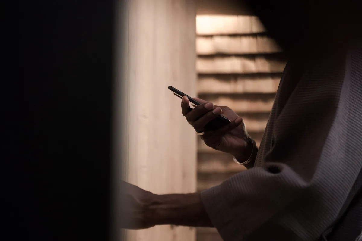A hand holding a phone in dim light, one of the common signs a husband is cheating