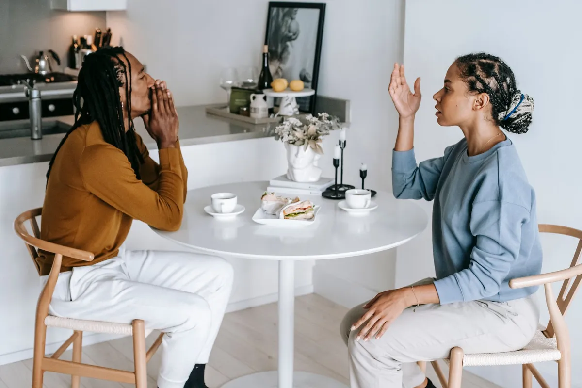 A couple at a kitchen table in a tense conversation about a lying husband