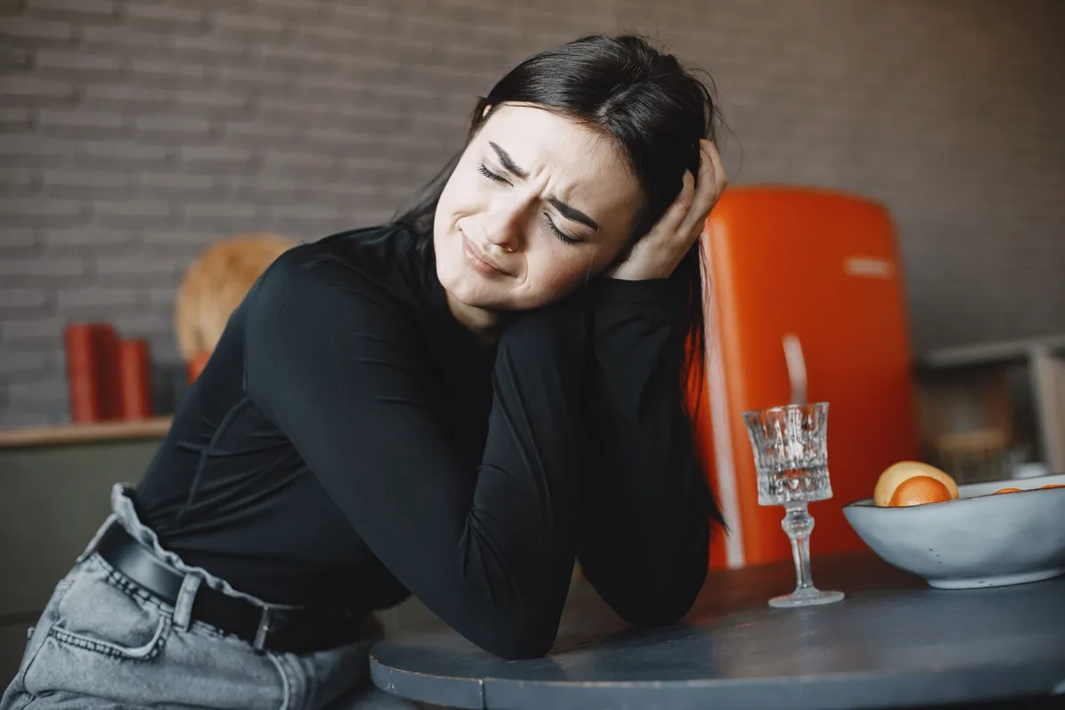 A woman leaning on a kitchen table with her eyes closed and her hand in her hair