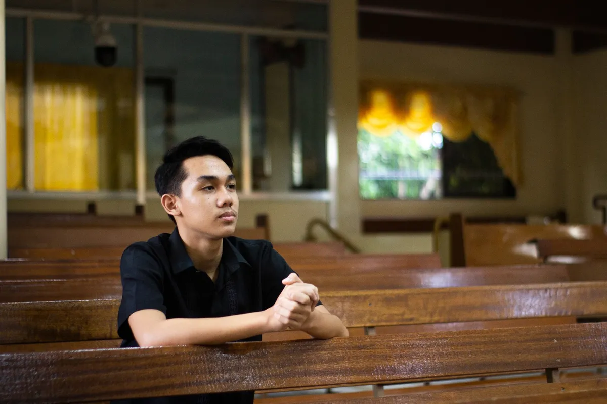 A man sitting alone in a church pew with his hands clasped