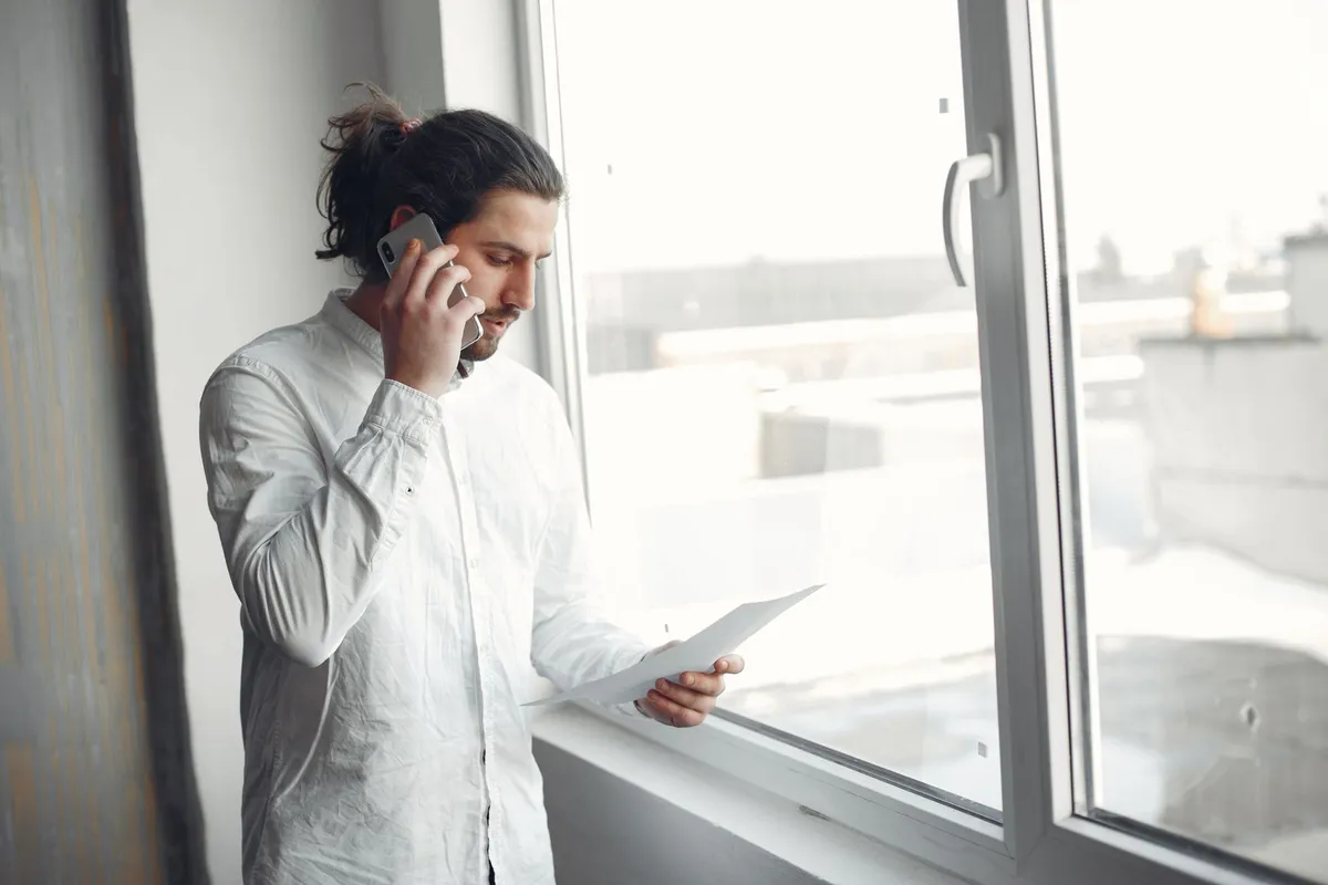 A man on a consultation phone call with a sex addiction therapist by a window in natural light