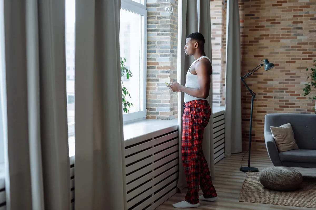 A man standing at a window in the morning holding a phone