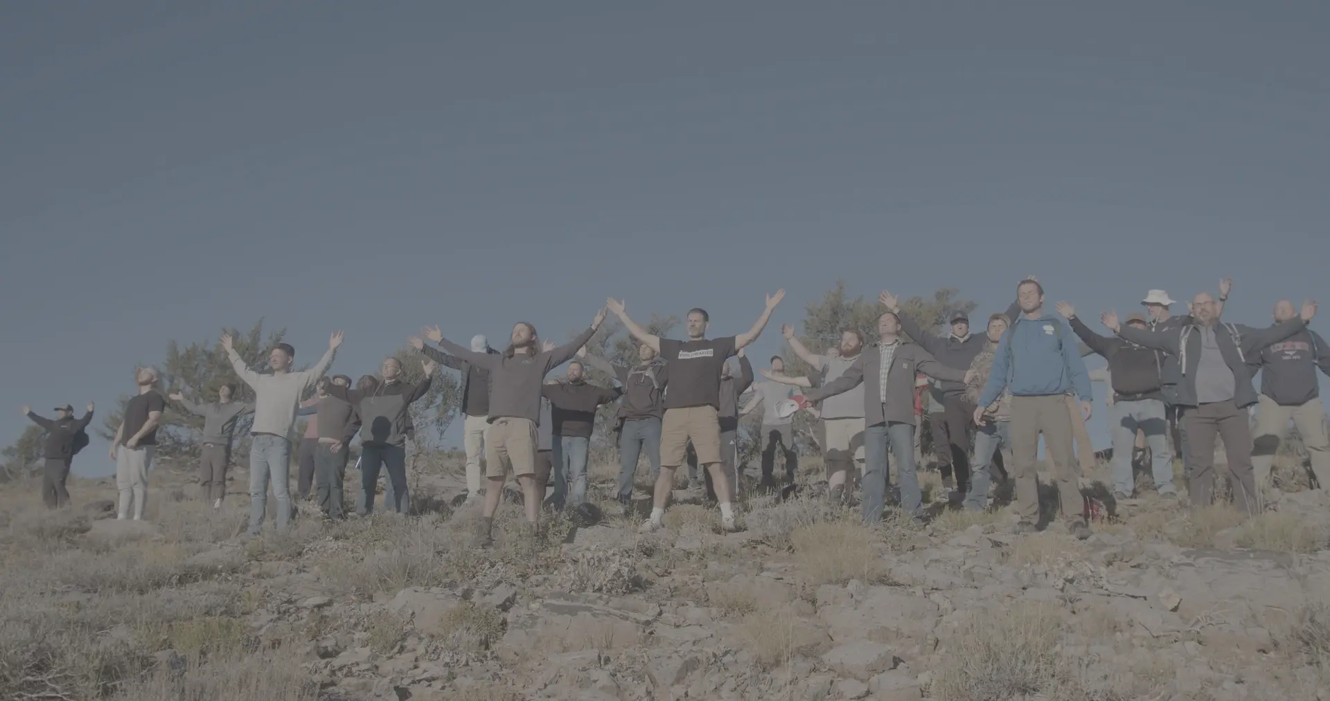 A group of men on a rocky hillside with their arms raised at a Rising Son retreat