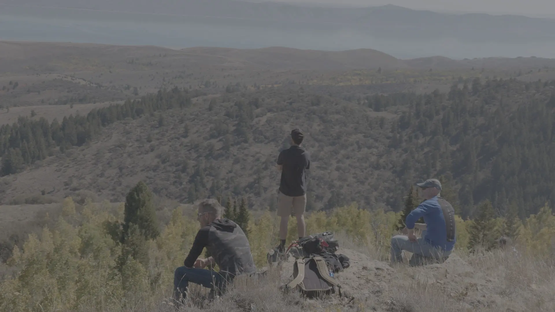 Three men resting on a ridge overlooking a wide mountain valley