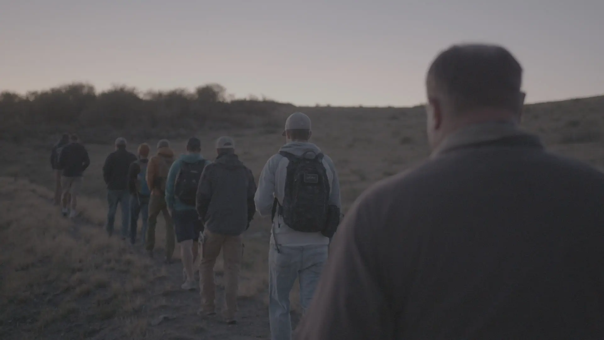 Men hiking single file across open high desert at dusk during a Rising Son retreat