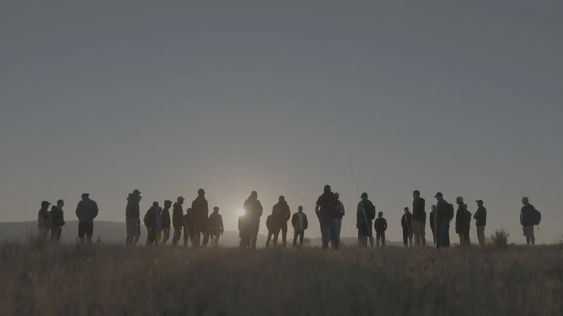 Silhouettes of men gathered along a ridge at sunrise during a Rising Son retreat